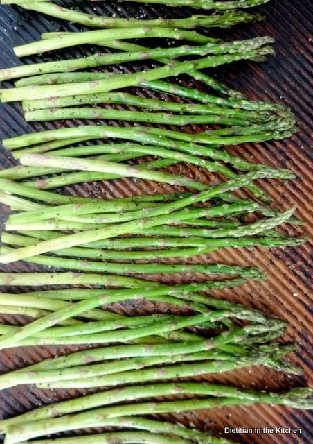 Asparagus spears on a baking sheet prepared for roasting with olive oil, salt and pepper. 