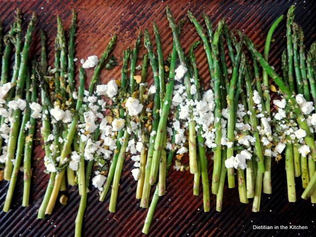 A sheet pan with roasted asparagus topped with feta cheese crumbles and basil pistachio gremolata.