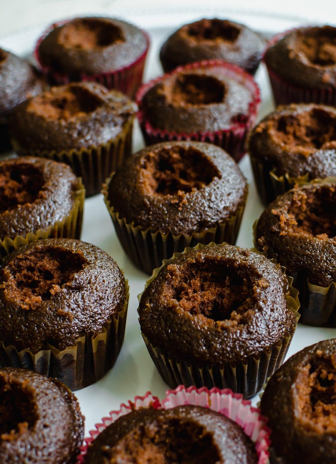 A close up shot of chocolate cupcakes on a white platter with the top of the cupcakes cut out in the center. 