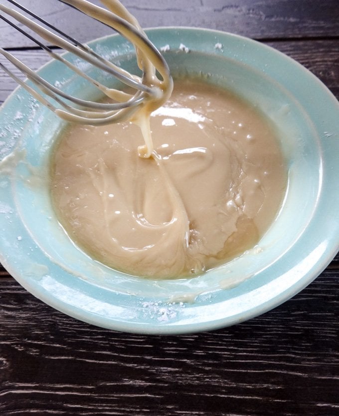 A whisk stirring maple donut glaze in a blue bowl. 