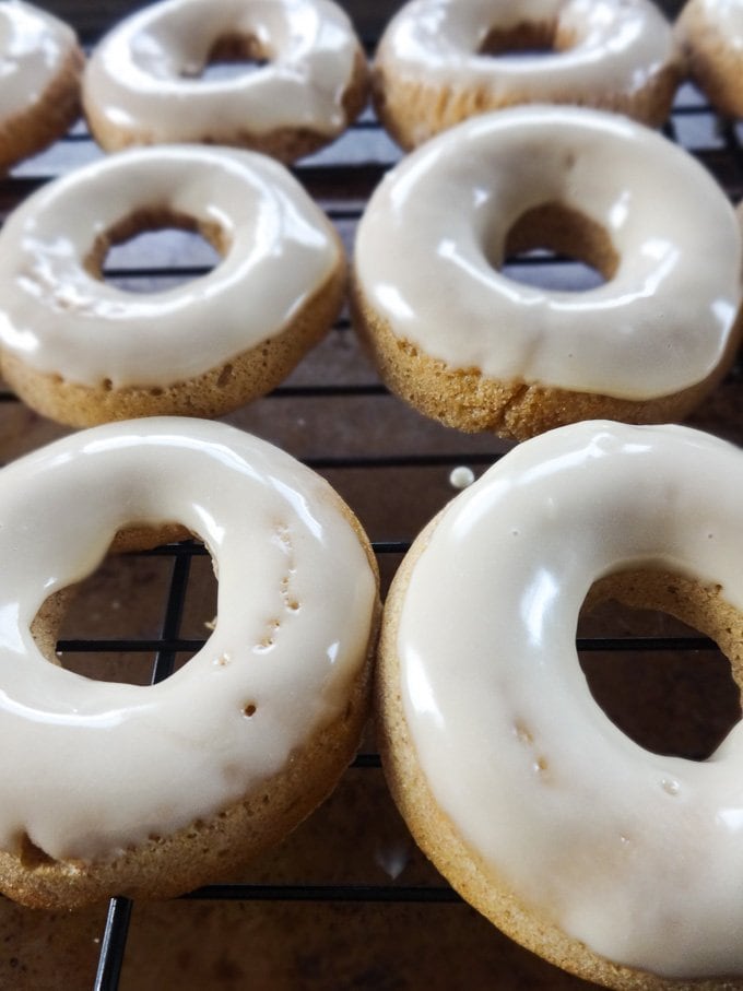 A close-up shot of apple cider donuts with maple glaze on a wire rack. 