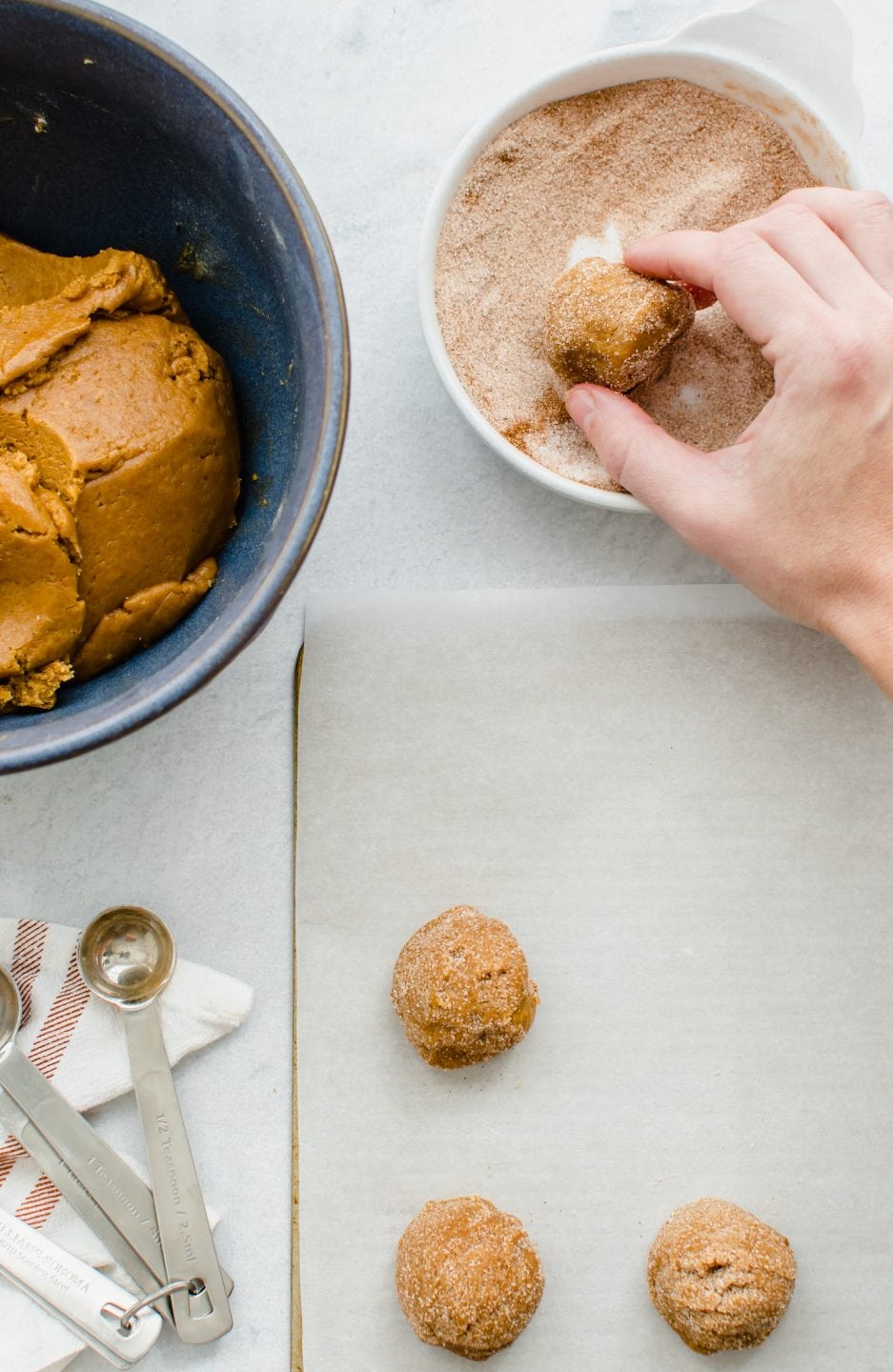 A hand rolling a cookie dough ball into cinnamon sugar.