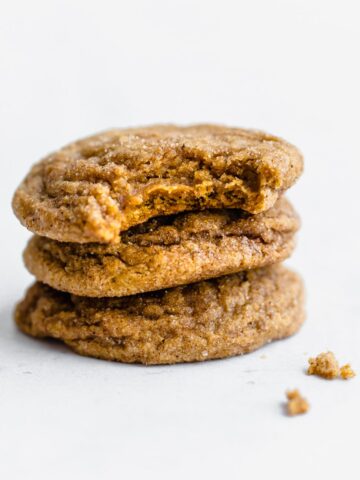 A stack of pumpkin cookie butter doodle cookies with a bite taken out of the top cookie.