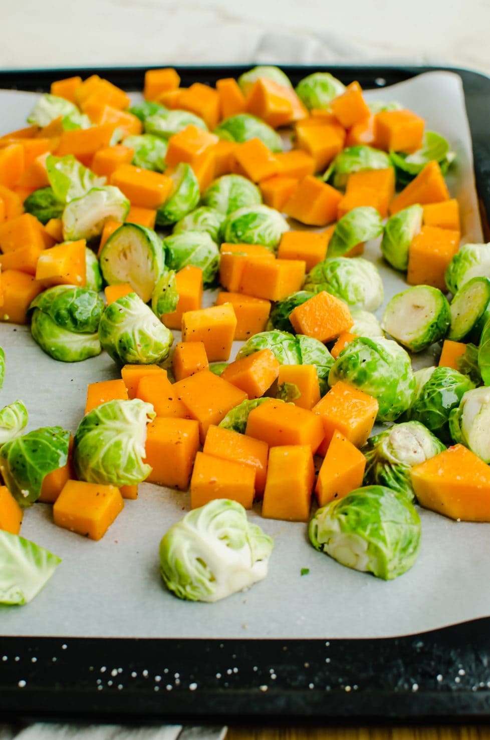 A baking sheet lined with parchment paper and filled with raw brussels sprouts and diced butternut squash.