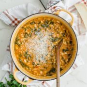 A yellow Dutch oven filled with 5-ingredient Italian bean stew that is stopped with shredded Parmesan cheese.