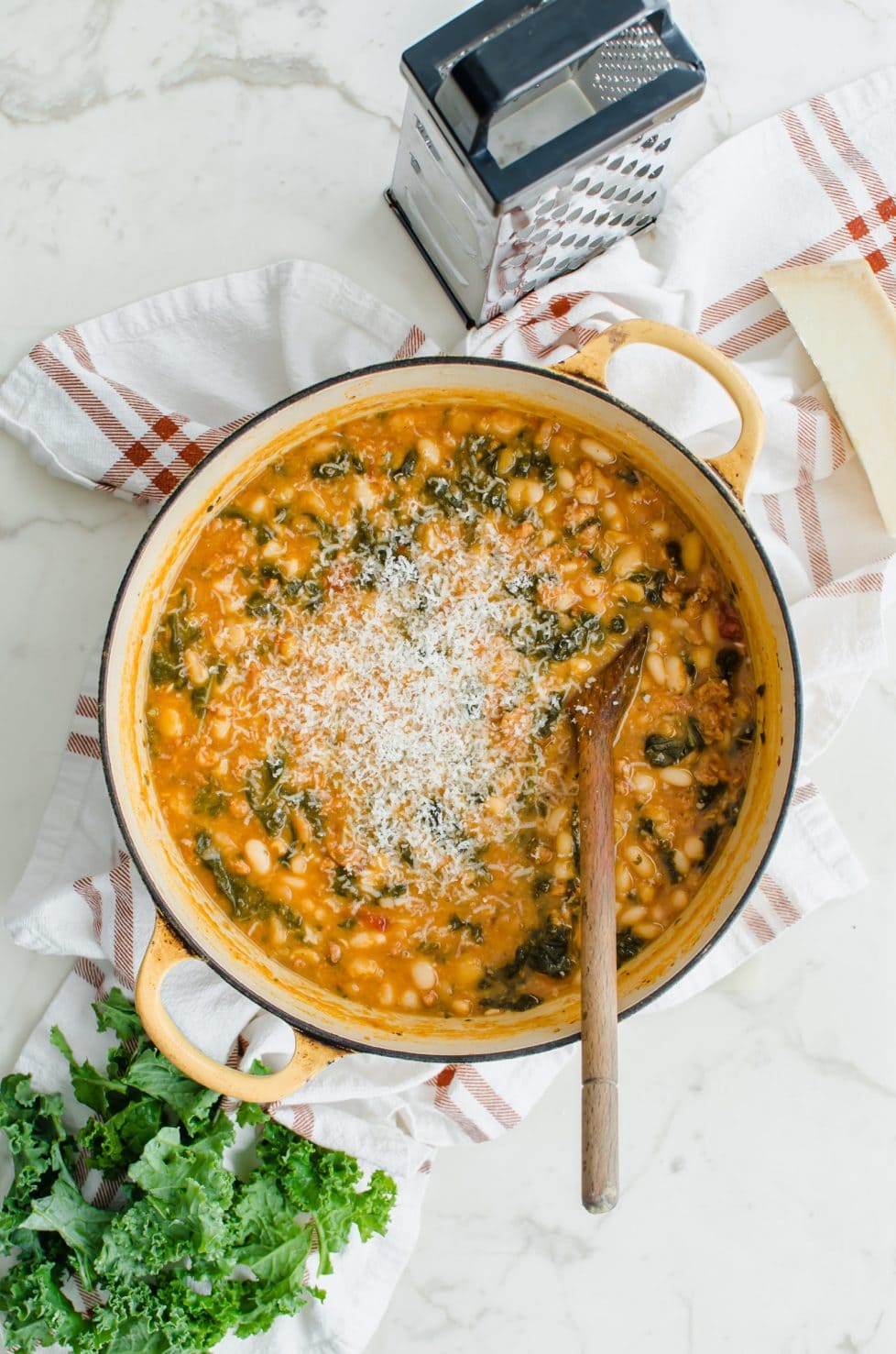 A yellow Dutch oven filled with 5-ingredient Italian bean stew that is stopped with shredded Parmesan cheese.