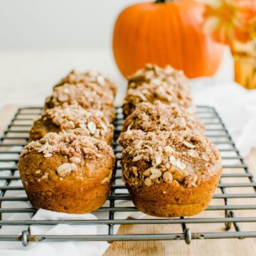 A cooling wire rack with pumpkin cream cheese streusel muffins and a pumpkin in the background.