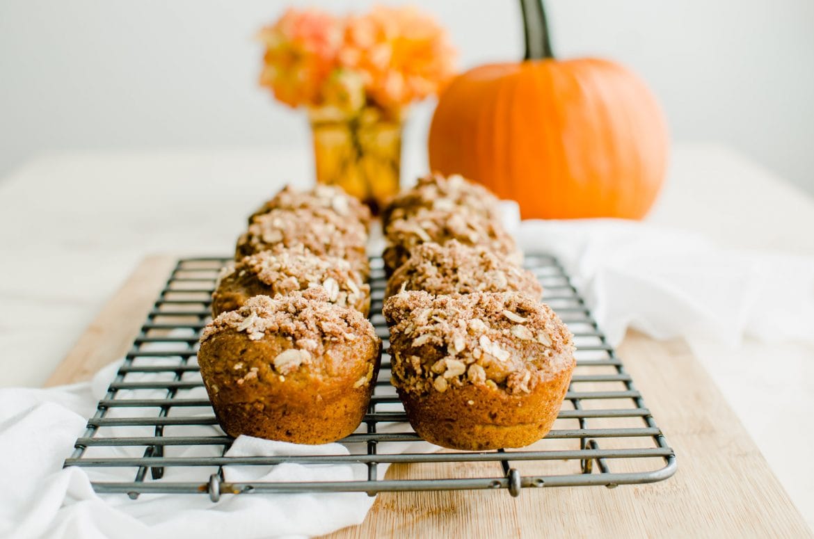 A cooling wire rack with pumpkin cream cheese streusel muffins and a pumpkin in the background.