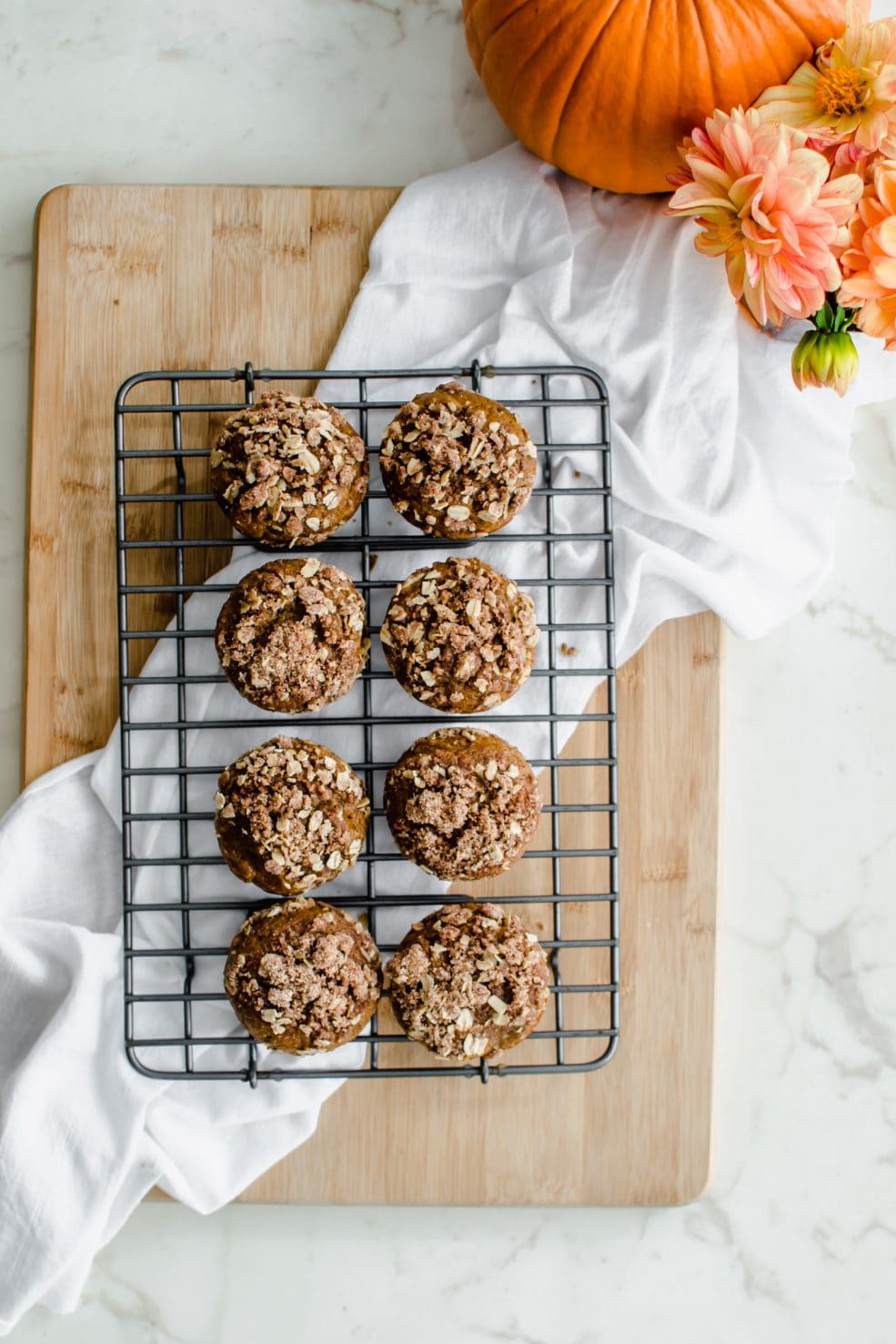 A cooling wire rack with pumpkin cream cheese streusel muffins and a pumpkin in the background.