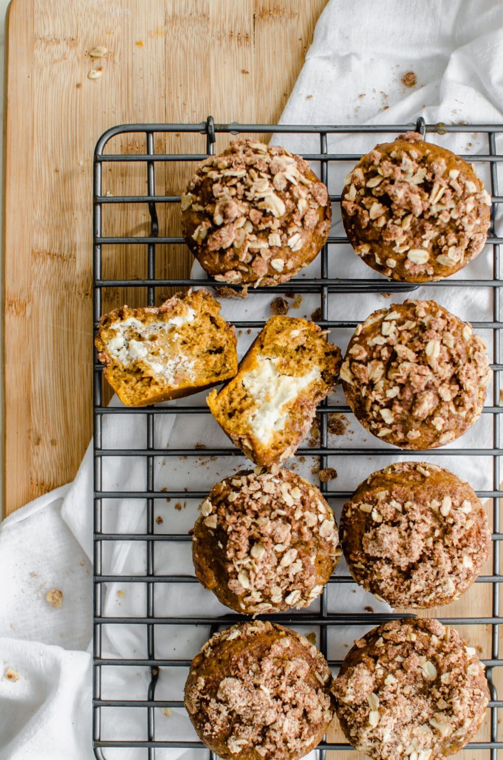 A wire cooling rack with pumpkin muffins on top and one muffin split open with cream cheese inside.