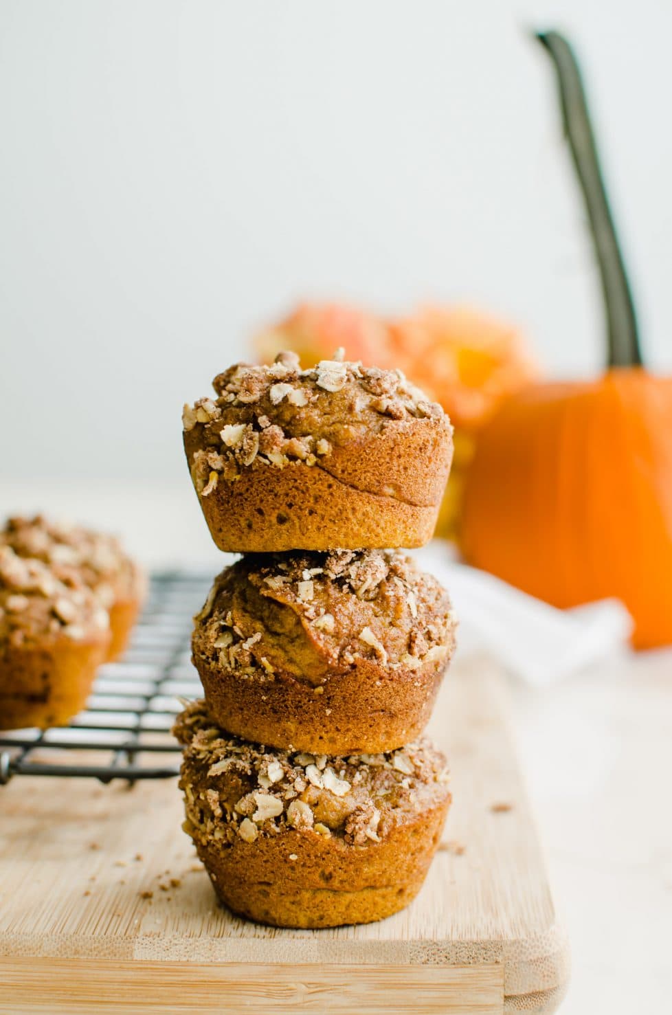 A stack of pumpkin cream cheese streusel muffins with a pumpkin in the background. 