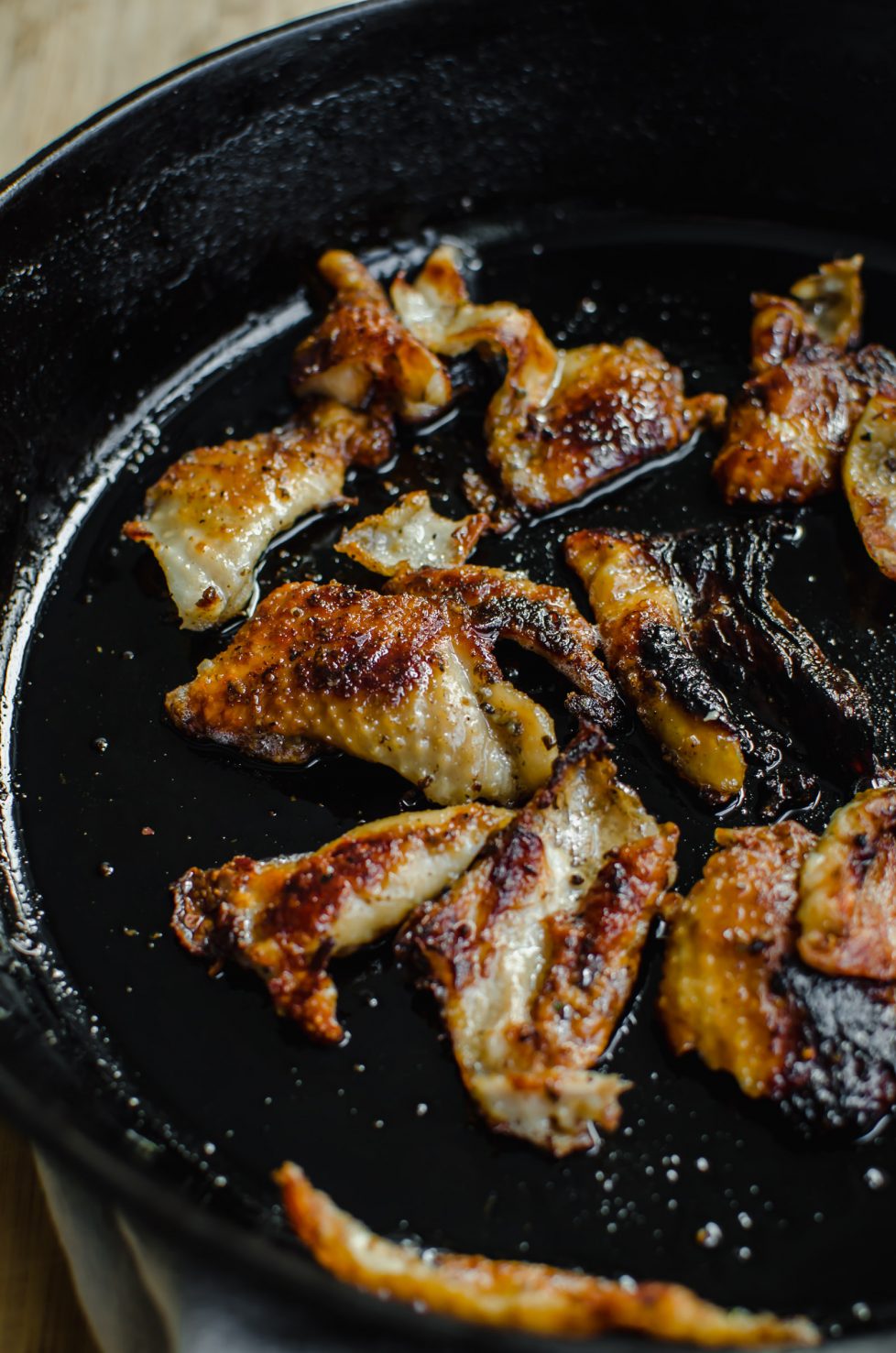 Pieces of turkey skin crisping in a cast iron skillet.