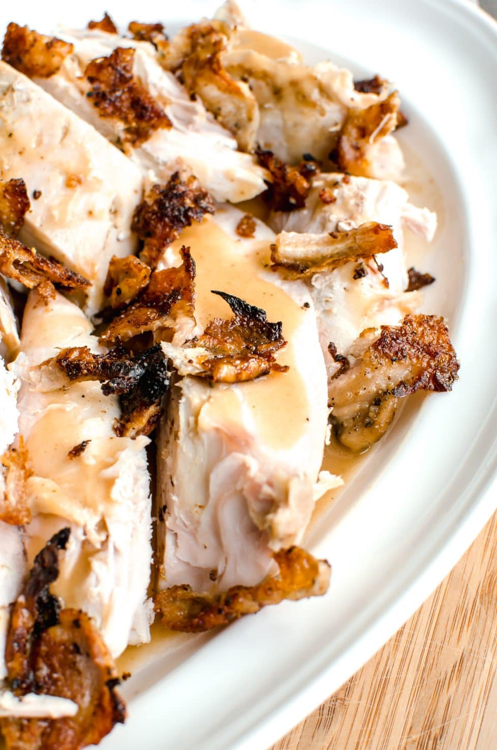 A white platter with pieces of turkey breast sitting on top of gravy with crispy skin on top.