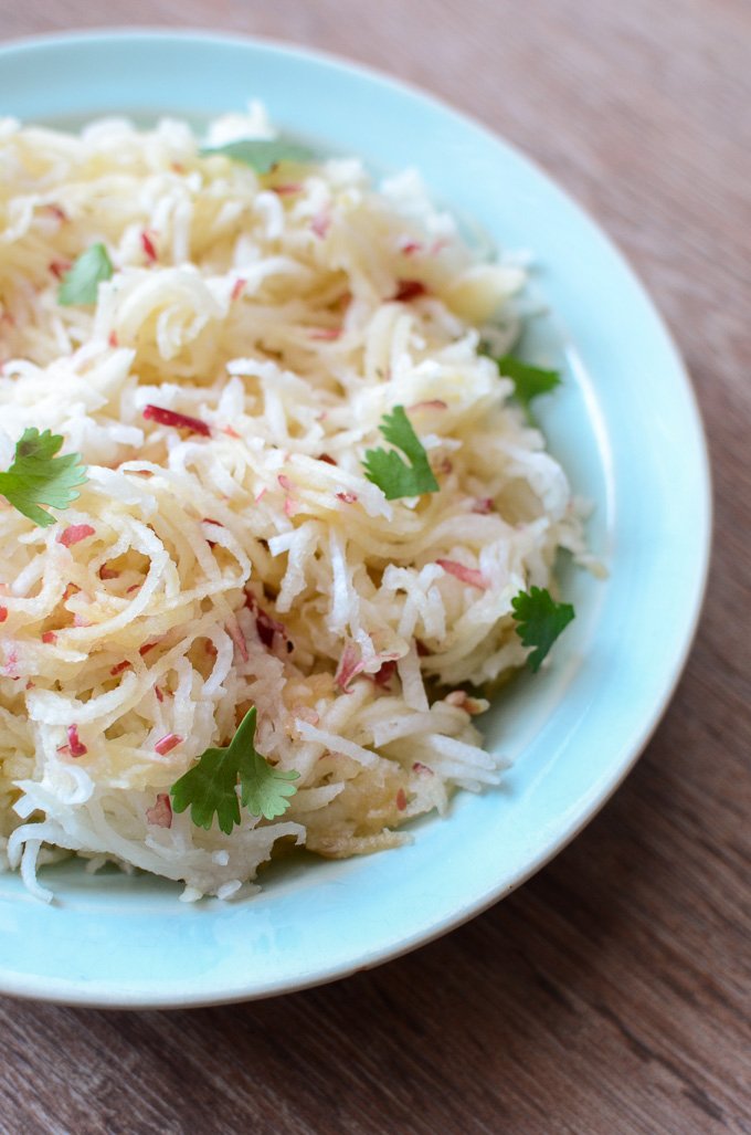 A side shot of grated apple jicama slaw in a blue bowl garnished with cilantro. 