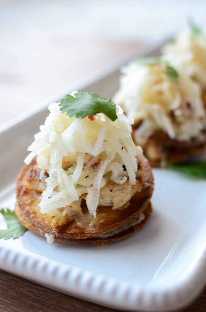 A close-up shot of mini chicken tostadas on a white platter garnished with slaw and cilantro. 