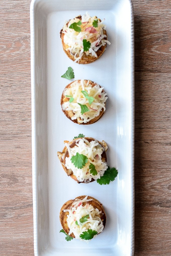 A row of mini Chicken Tostadas garnished with slaw and cilantro on a rectangular white serving platter. 