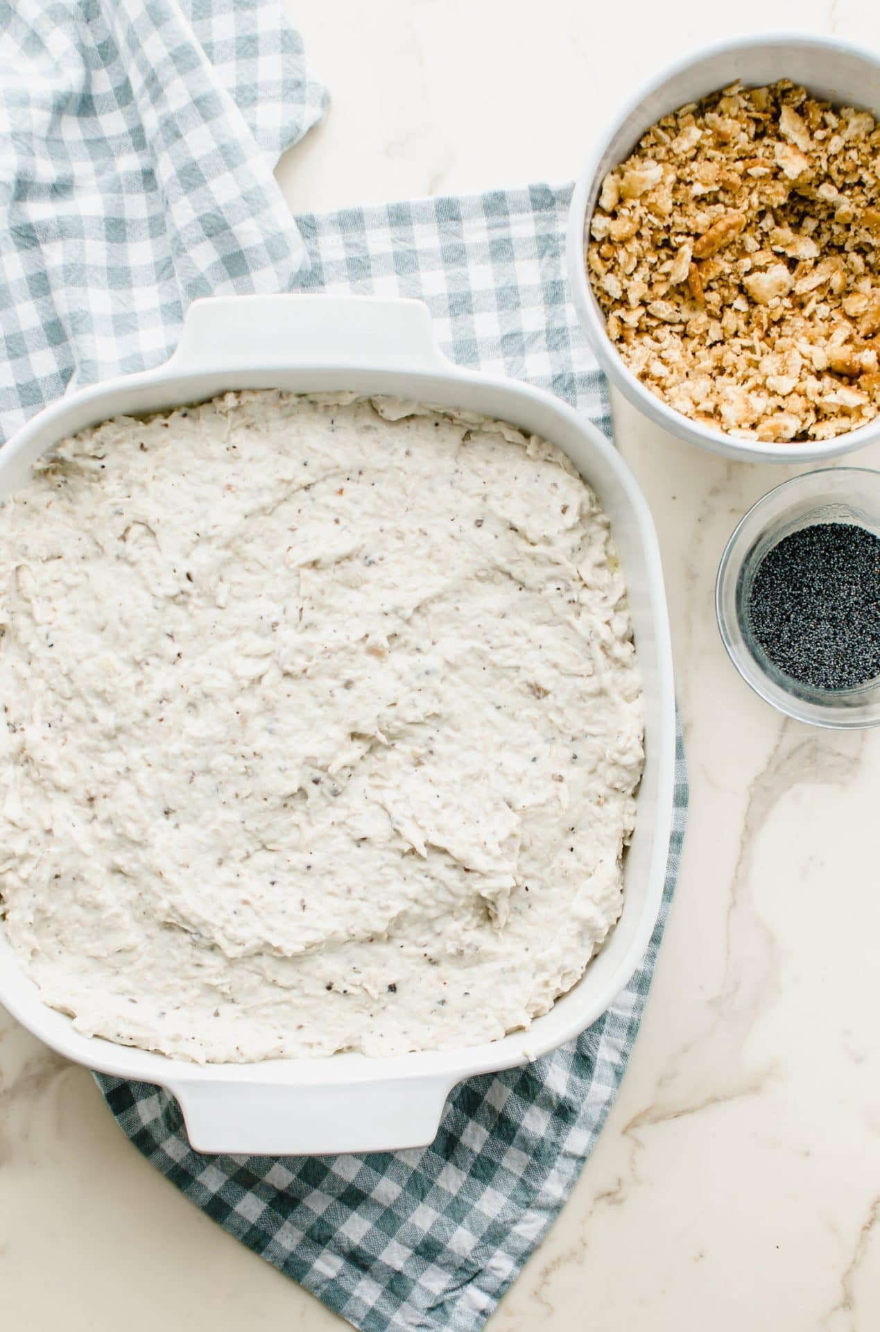 Poppy seed chicken casserole in a white dish with a bowl of crushed crackers on the side.