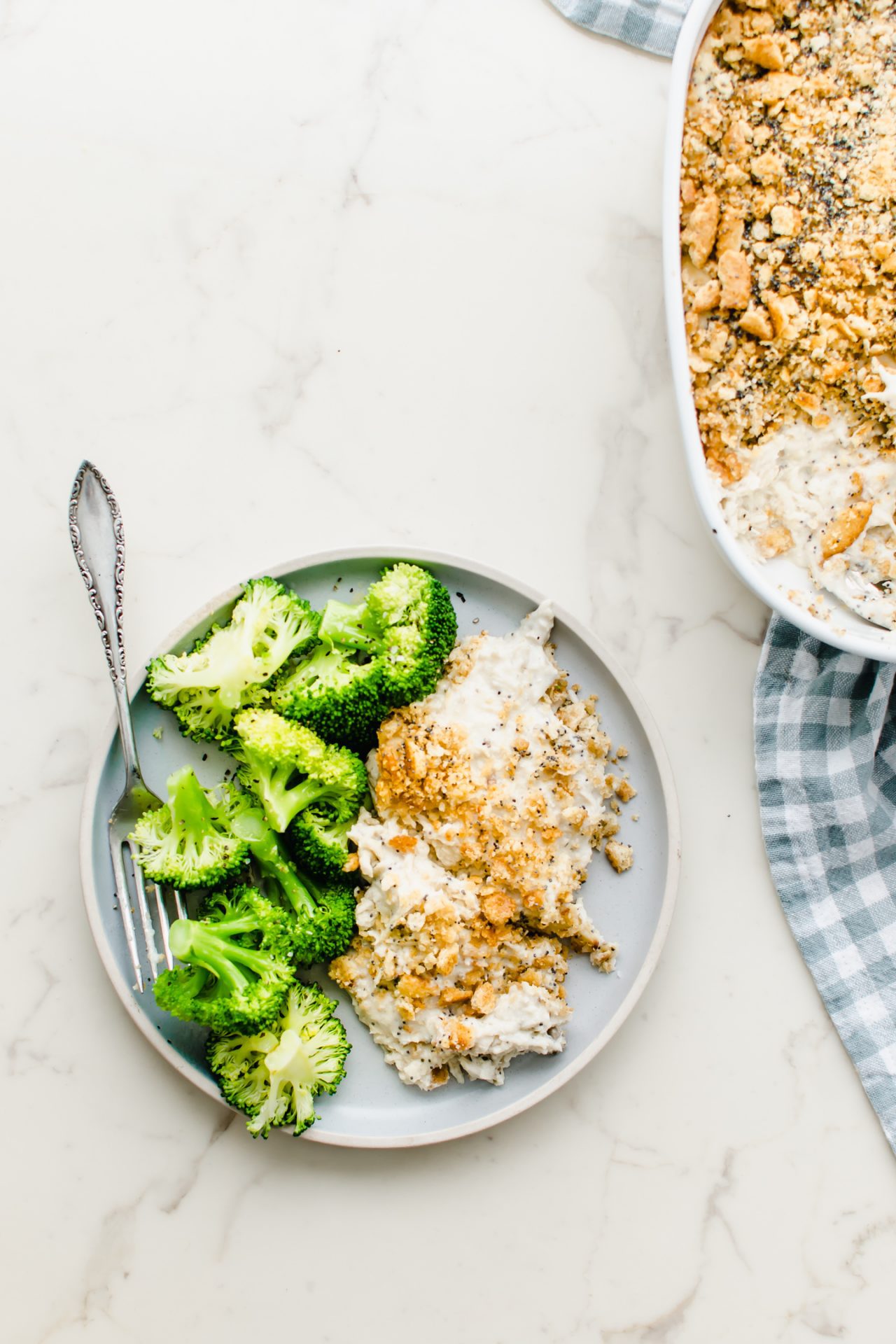 A serving of poppy seed chicken on a blue plate with broccoli on the side.