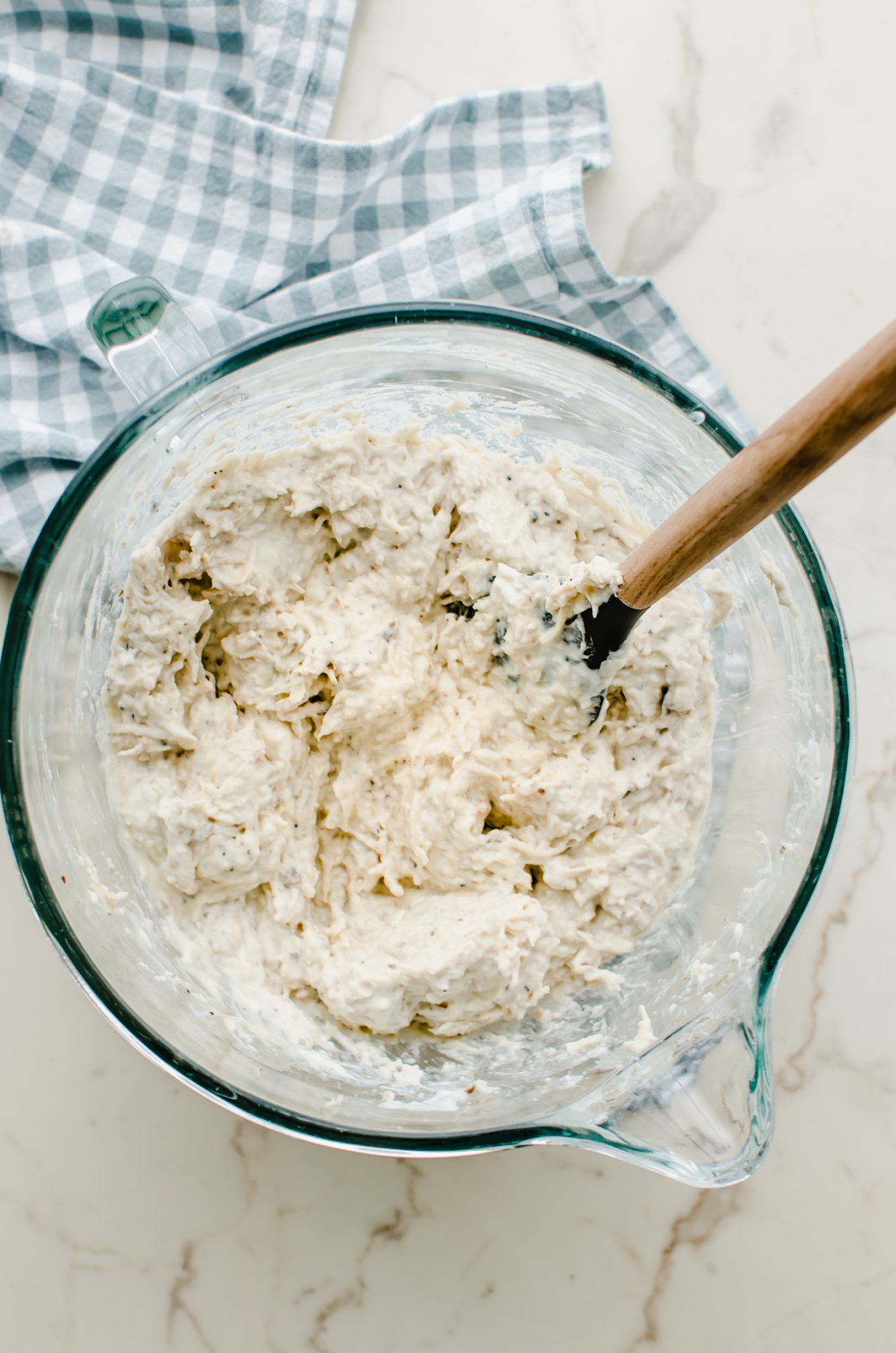 Poppy seed chicken in a mixing bowl with a rubber spatula.