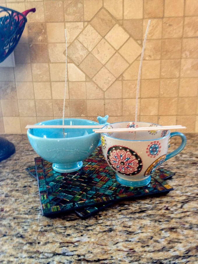 Coffee Cups with wicks held in place by small sticks across the tops of the cups. There is no wax in the cups yet.