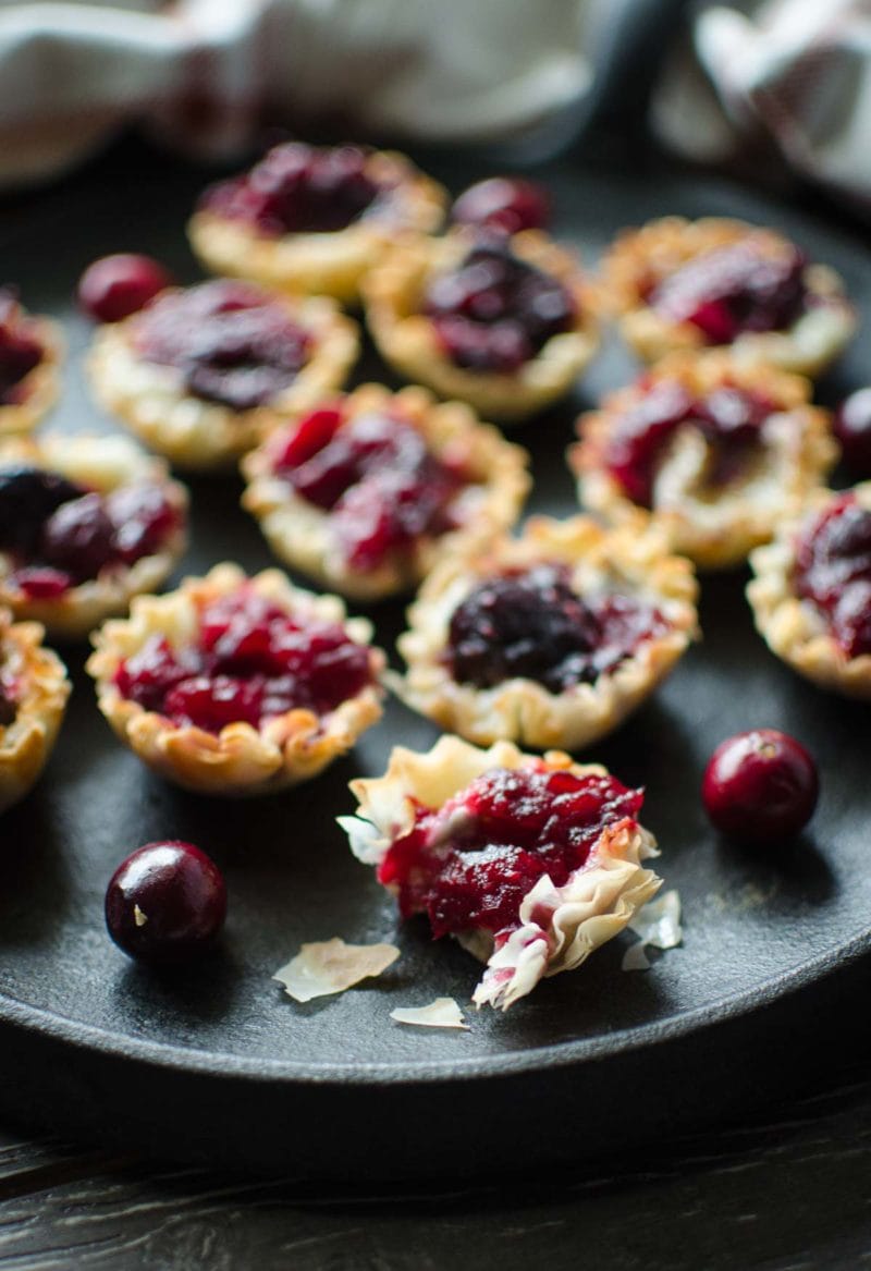 A tray of cranberry brie tartlets with fresh cranberries on the side. 