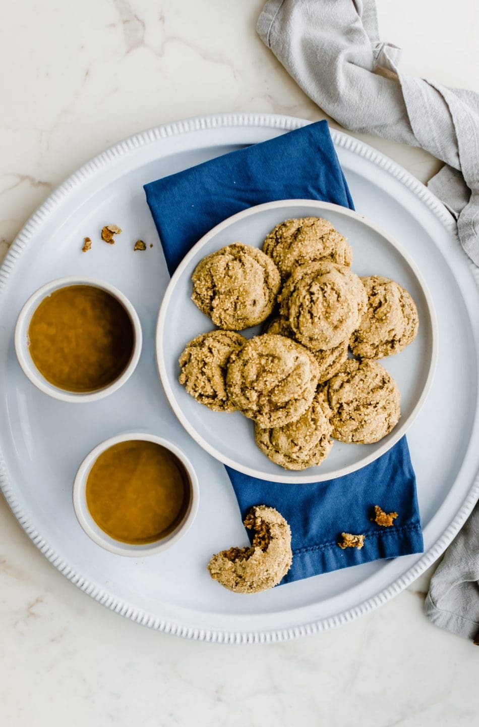 Two blue stone cups of spiced tea on a white platter with a plate of ginger cookies on the side.