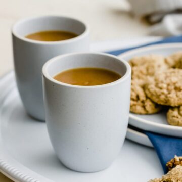 Two blue stone cups of spiced tea on a white platter with a plate of ginger cookies on the side.