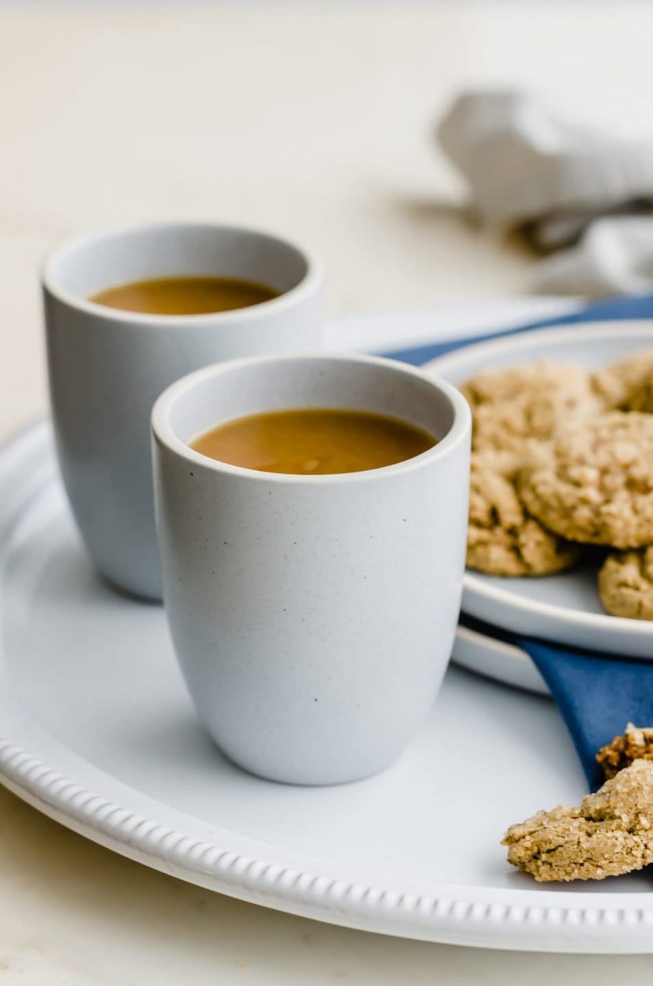 Two blue stone cups of spiced tea on a white platter with a plate of ginger cookies on the side.