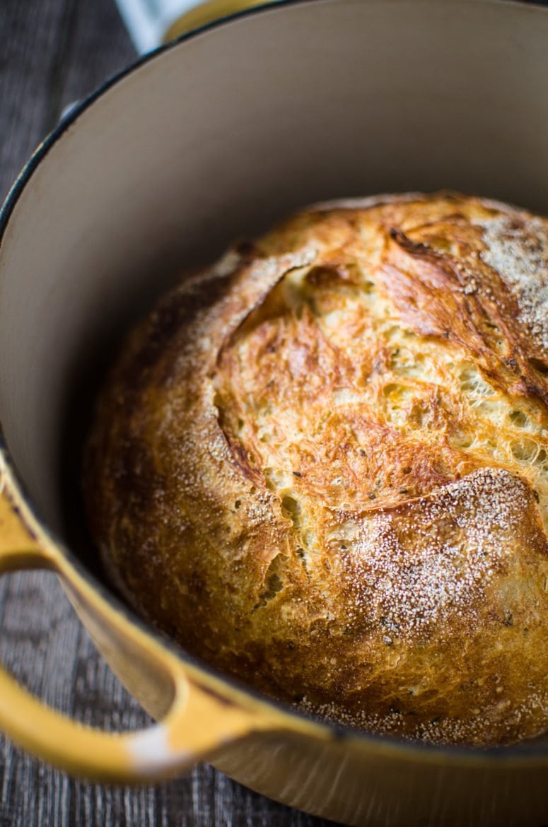 A close up of a yellow Dutch oven with a bread boule inside on a wood background. 