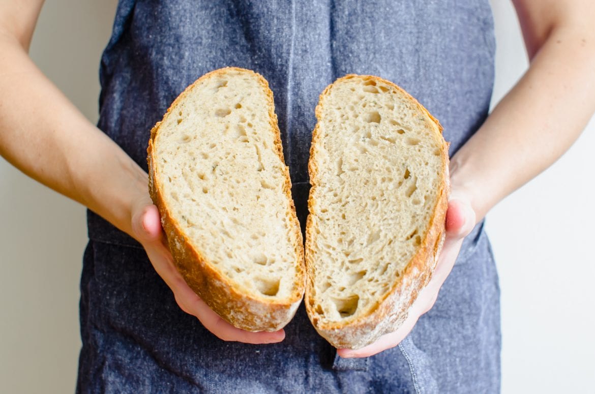 A women's hands holding a bread boule broken in half. 
