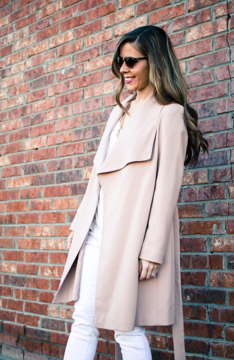 A chic spring look featuring a neutral color palette of a blush trench coat, white blouse, white jeans, and taupe sandals. Style and fashion inspiration for women.