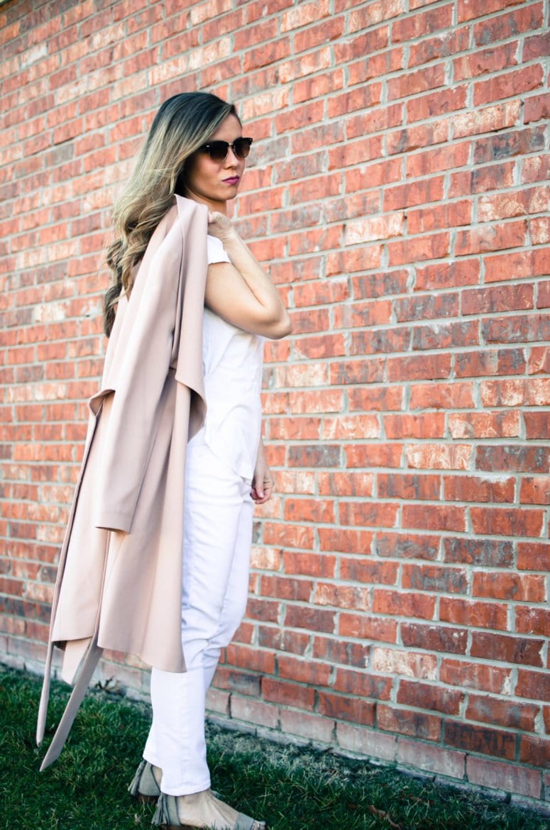 A chic spring look featuring a neutral color palette of a blush trench coat, white blouse, white jeans, and taupe sandals. Style and fashion inspiration for women.