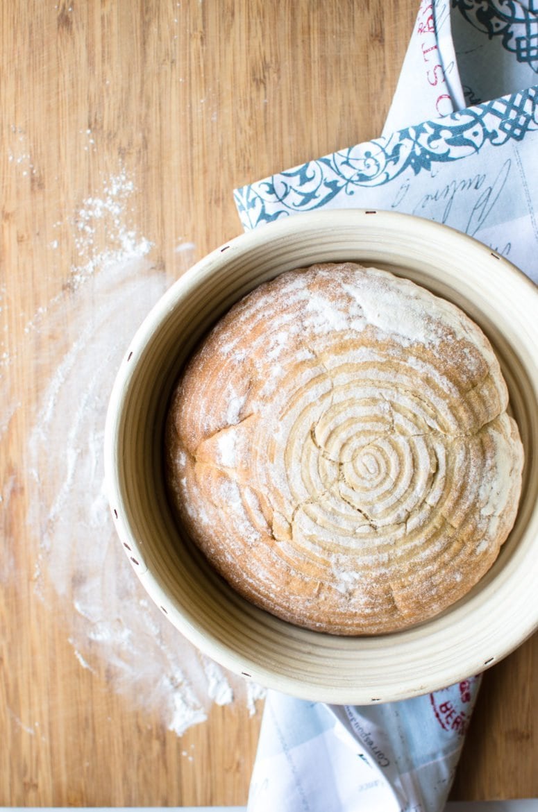 A cooked loaf of sourdough bread in a bread basket.