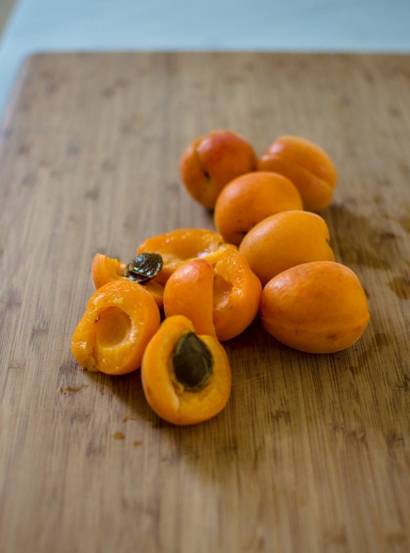 A few apricots on a cutting board. Some are cut and others are whole. 