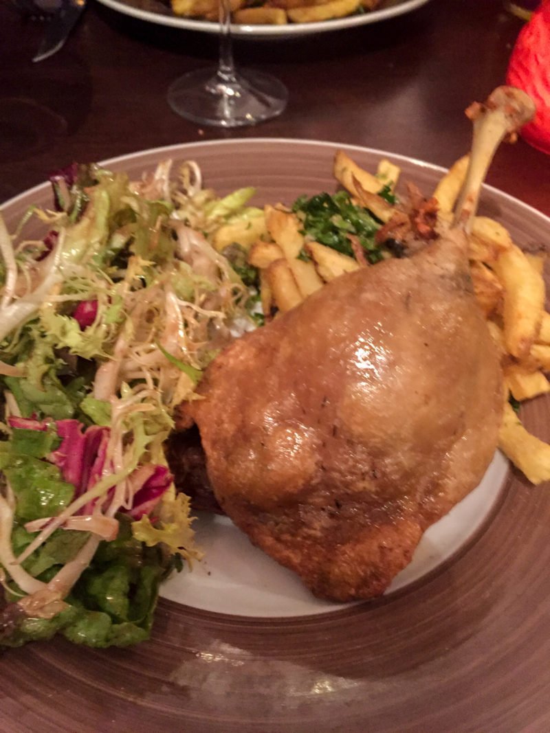 Crispy duck leg with a fresh salad and garlic parsley frites in Paris, France