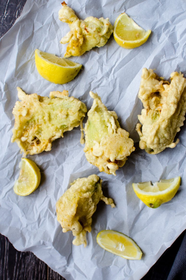 Fried zucchini blossoms on parchment paper with lemon wedges. 