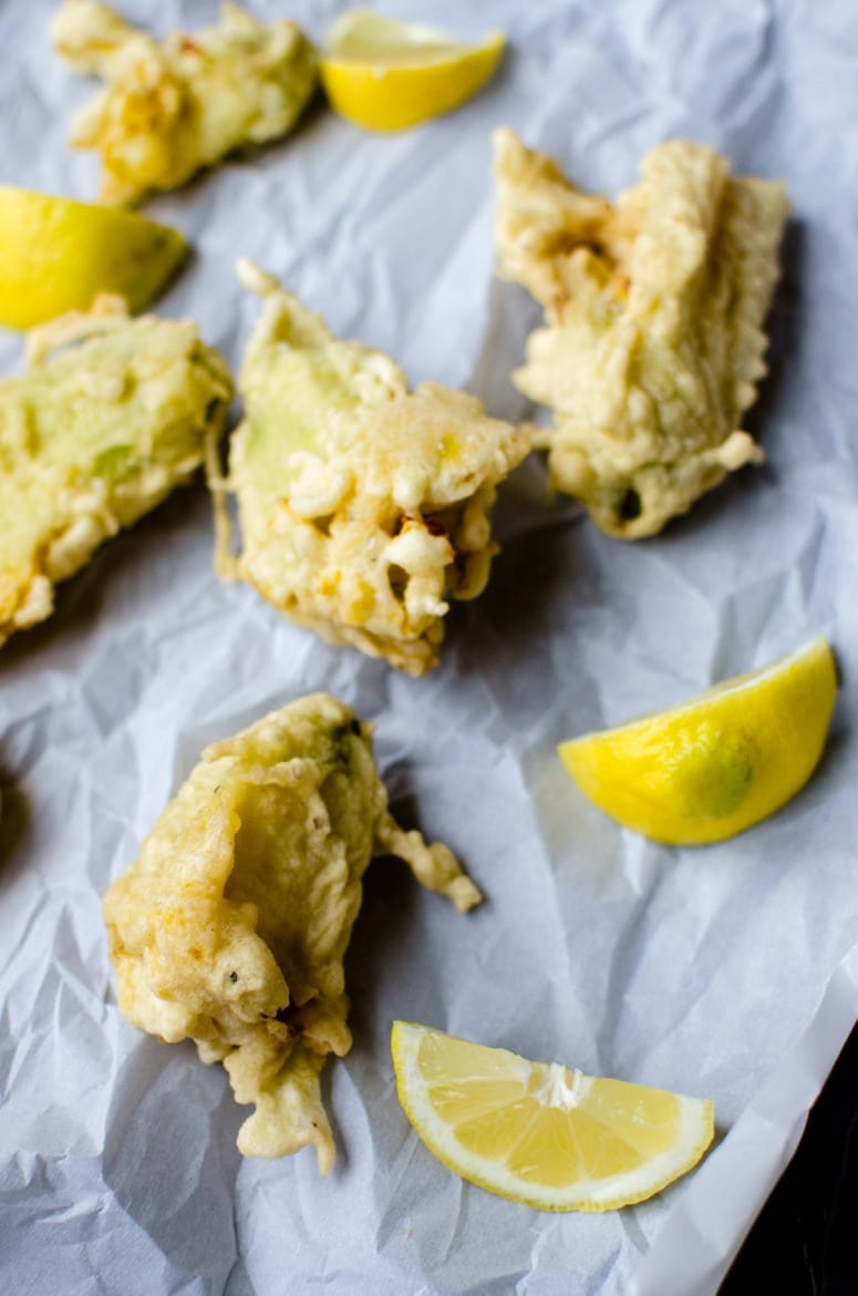 Fried zucchini flowers on parchment paper with lemon wedges on the side. 