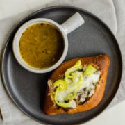 An overhead shot of an Italian beef sandwich on a grey plate with a cup of au jus on the side.