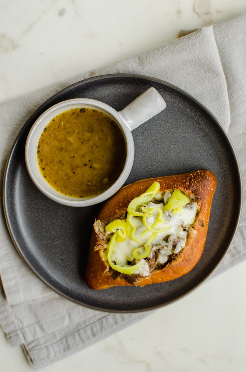 Italian beef sandwich on a plate next to dipping sauce.