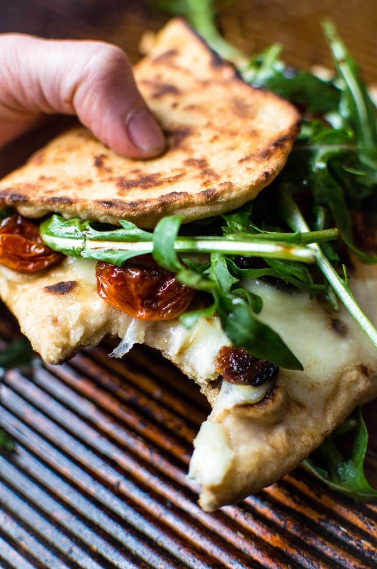 A piece of BLT Naan pizza folded over with a bite taken from it. 