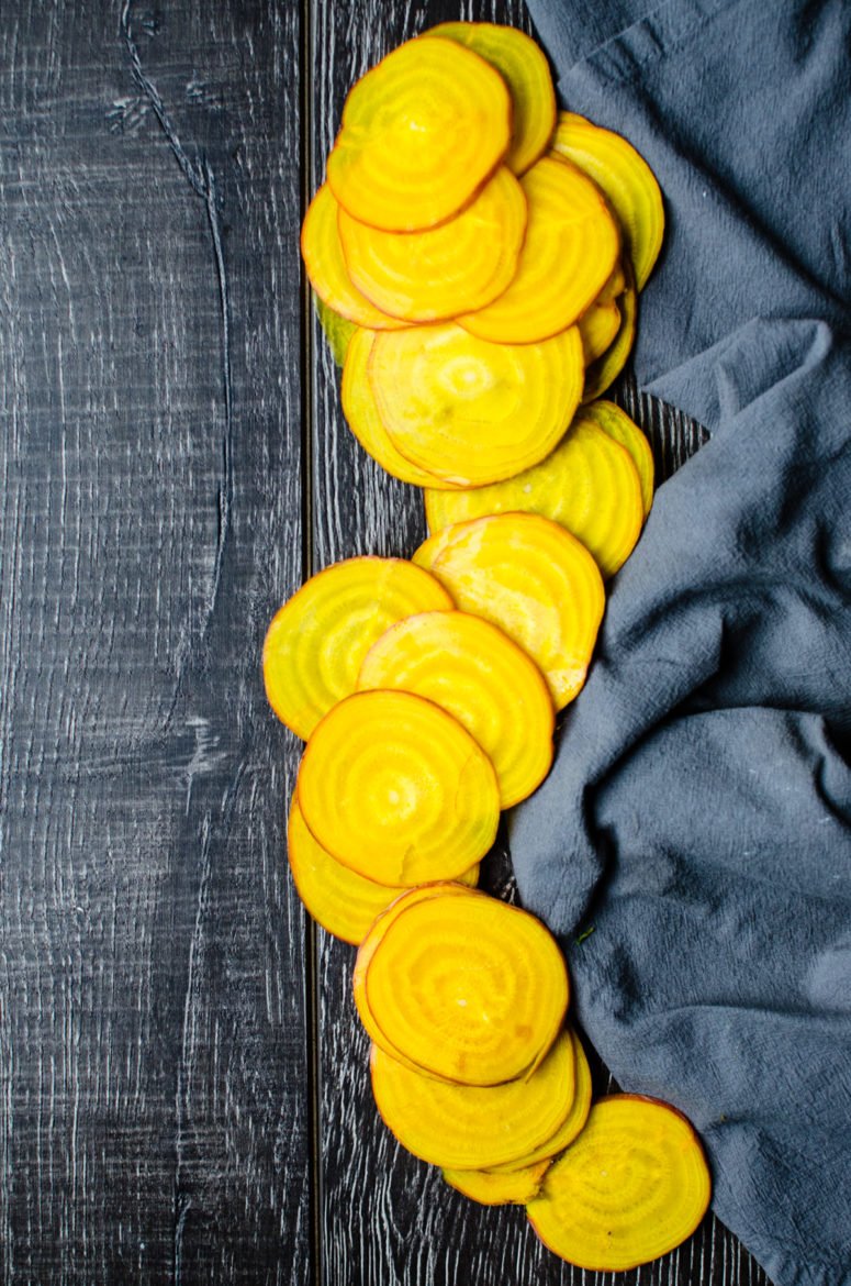 Thin slices of yellow beet on a blue dish towel. 