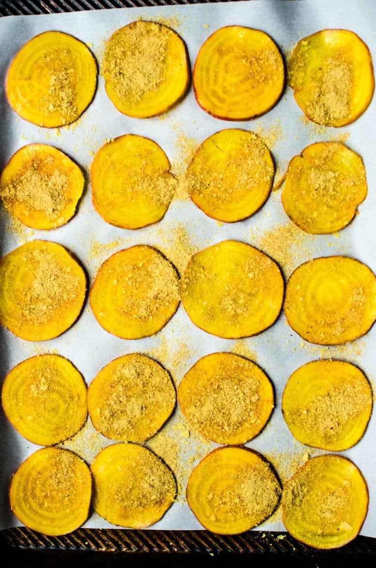 Slices of beet on parchment paper sprinkled with nutritional yeast seasoning. 