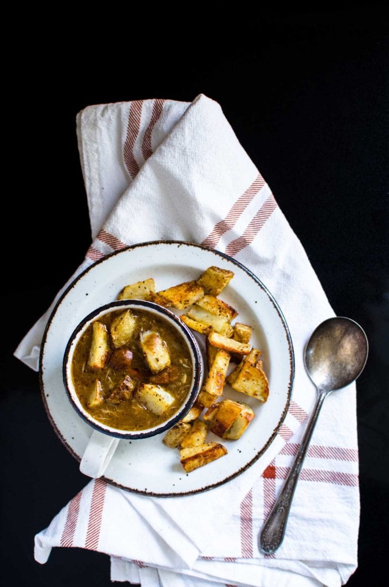 Overhead view of a cup of gumbo on a plate of crispy potatoes. 