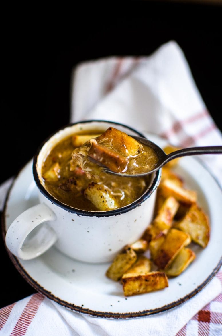 A spoon taking a bite of gumbo from a full cup of gumbo. 