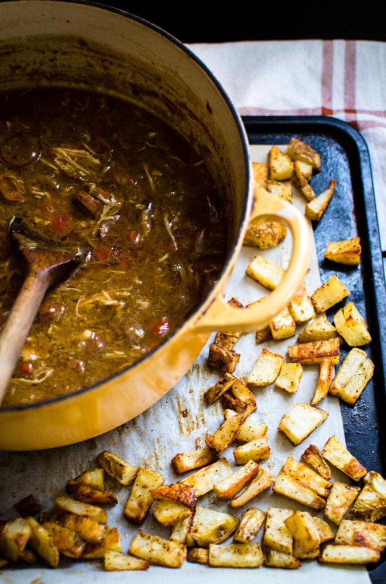 A pot of gumbo viewed over a pan of crispy potato pieces.