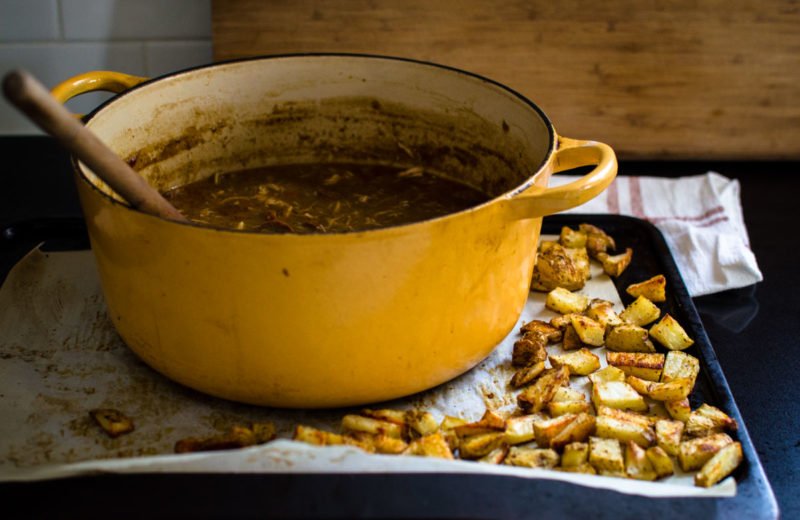 Side view of a pot of gumbo and a tray of crispy potato pieces. 