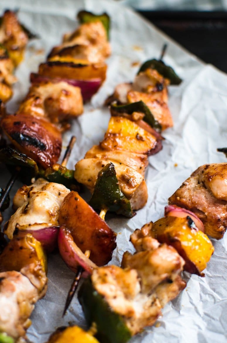 A close up shot of grilled peach bbq chicken kabobs against a sheet of parchment paper. 
