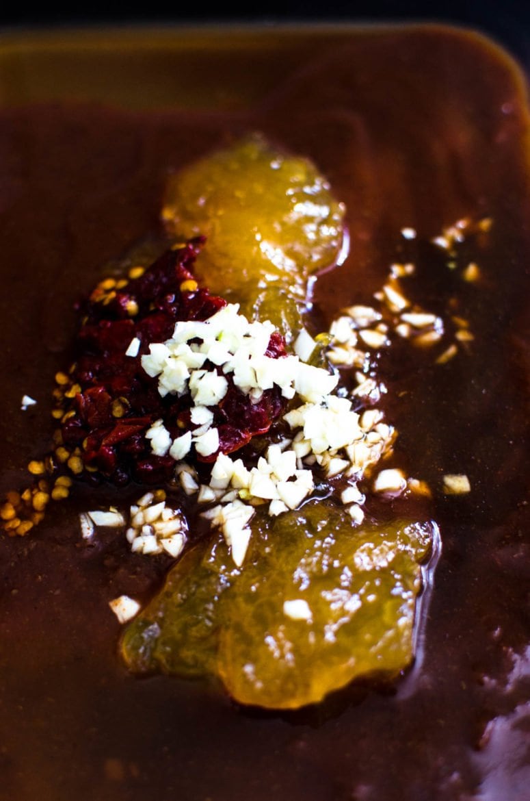 A close up shot of garlic, peach jam, bbq sauce, and spices in a plastic container. 