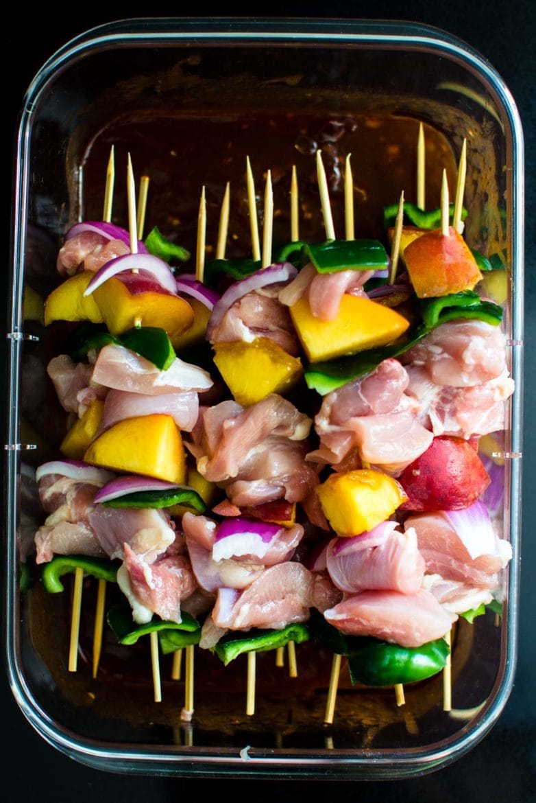 A Rubbermaid Brilliance container with Peach BBQ Marinade and chicken kabob skewers. 