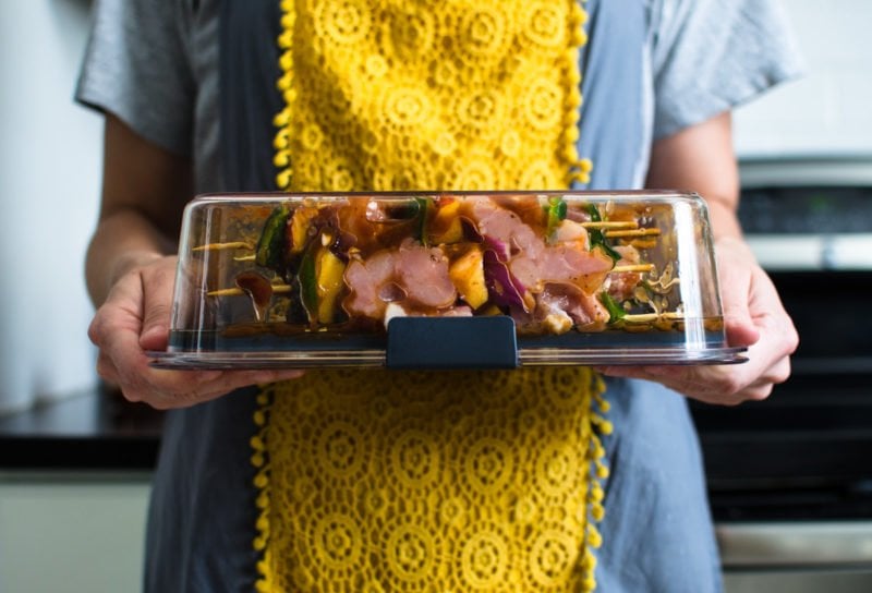 A woman turning a container of marinated chicken kabobs upside down to demonstrate that the container does not leak.